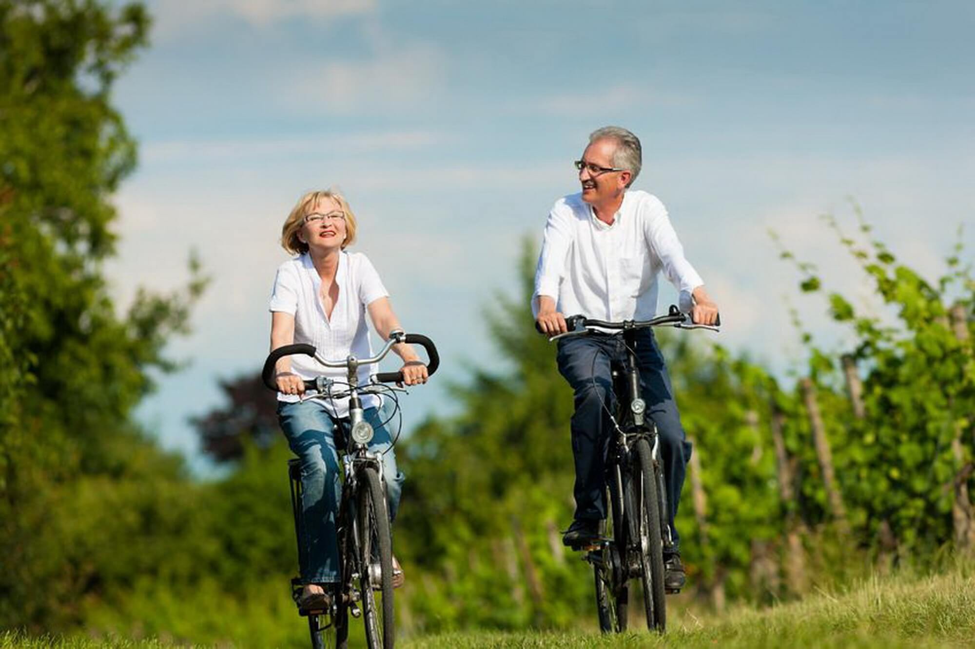Középkorú házaspár kerékpározik egy dűlőn a napsütésben