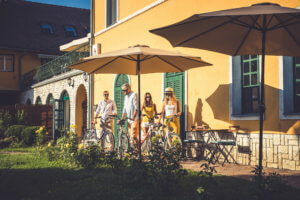 Egy társaság napsütésben kerékpárokat parkol le a villánykövesdi Hotel Cabernet mellett
