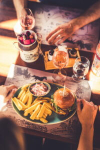 Kézműves hamburger felülnézetből sültkrumplival és coleslow-val tálalva egy asztalon, mellette roséval töltött borospoharak