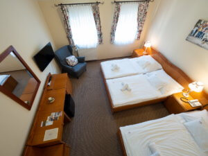 A Hotel Cabernet standard háromágyas szobája, a képen egy dupla ágy és egy külön ágy, tévé, íróasztal, fotel